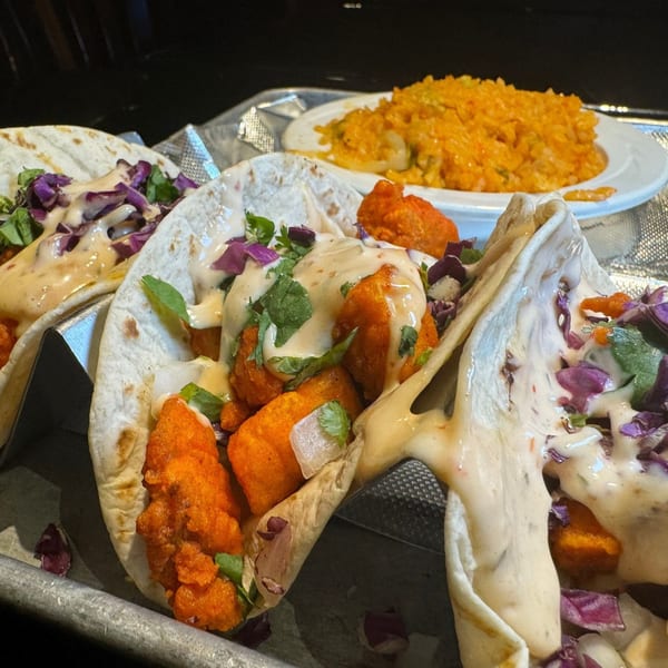 Three buffalo chicken tacos with purple cabbage, cilantro, and creamy sauce, with a side of rice.