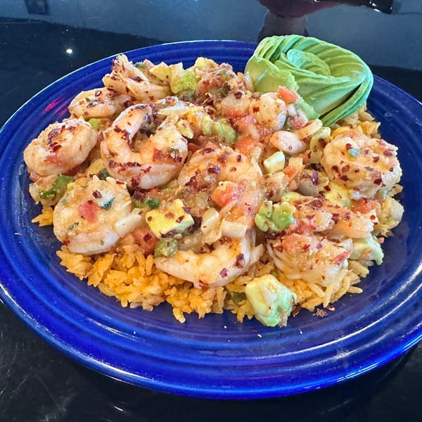 Shrimp and rice dish with avocado and tomato salsa, served on a vibrant blue plate.