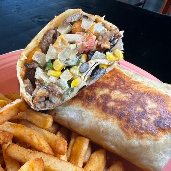 A grilled burrito, cut in half to show its filling, served with a side of golden french fries.