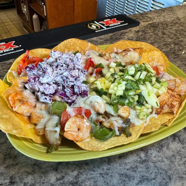 Shrimp nachos with melted cheese, red cabbage slaw, and green salsa on a lime green plate.