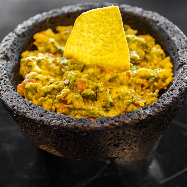 Fresh guacamole with a tortilla chip in a dark stone molcajete.